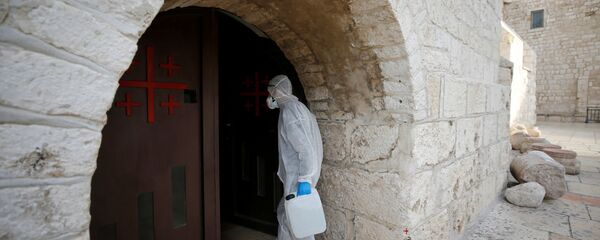 عامل يرتدي بدلة واقية يصل لتطهير كنيسة المهد كإجراء وقائي ضد فيروس كورونا في بيت لحم في الضفة الغربية التي تحتلها إسرائيل - سبوتنيك عربي