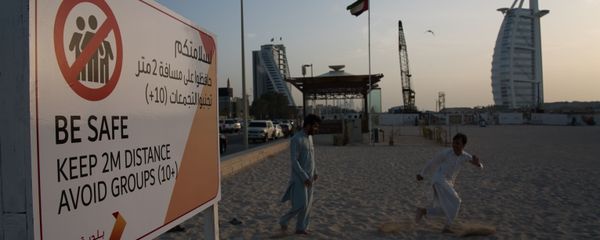 عاملان يلعبان بالقرب من لافتة تحذر الناس بضرورة الحفاظ على مسافة من بعضهم البعض عند تفشي الفيروس التاجي الجديد أمام فندق برج العرب الفاخر على شكل شراع في دبي - سبوتنيك عربي