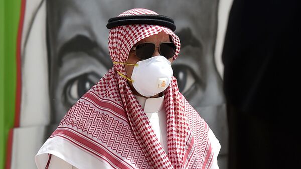 مواطن سعودي يرتدي قناعًا وقائيًا كإجراء احترازي ضد فايروس كورونا، يسير أمام لوحة جدارية تظهر وجه الملك سلمان بن عبد العزيز ، في العاصمة الرياض ، 15 مارس 2020.  - سبوتنيك عربي