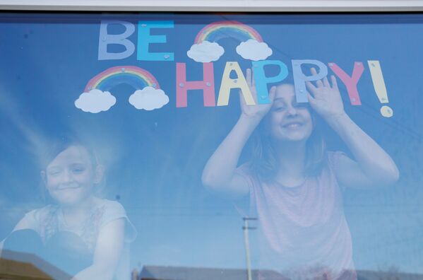 الفتاتان صوفي وإميلي وارد، خلف زجاد نافذتهما عليها رسالة كن سعيدا! في سانت هيلينز ، مع استمرار انتشار مرض فيروس التاجي (COVID-19). سانت هيلينز، بريطانيا، 25 مارس 2020 - سبوتنيك عربي