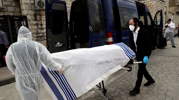 عمال جمعية الدفن اليهودية يرتدون ملابس واقية أثناء حملهم جثة ضحية لمرض فيروس كورونا لدفنه في القدس - سبوتنيك عربي