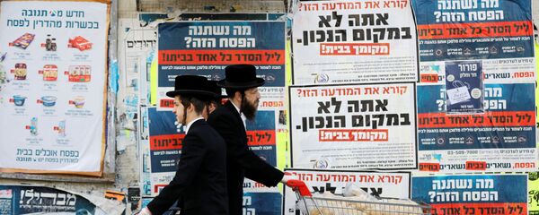 رجال اليهود الأرثوذوكس يدفعون عربات أثناء مرورهم على خلفية لوحات إعلانية تحث الناس على البقاء في منازلهم والالتزام بالاجراءات الحكومية لمنع  تفشي مرض فيروس التاجي (COVID-19) في أشدود، إسرائيل، 1 أبريل 2020. - سبوتنيك عربي