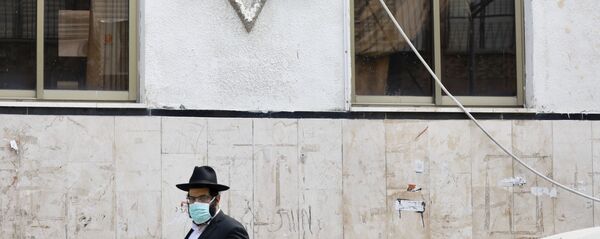 رجل متشدد يمشي بالقرب من كنيس يهودي في شارع مهجور بسبب الإجراءات الحكومية للمساعدة في وقف انتشار فيروس كورونا في بني براك إحدى ضواحي تل أبيب في إسرائيل  - سبوتنيك عربي