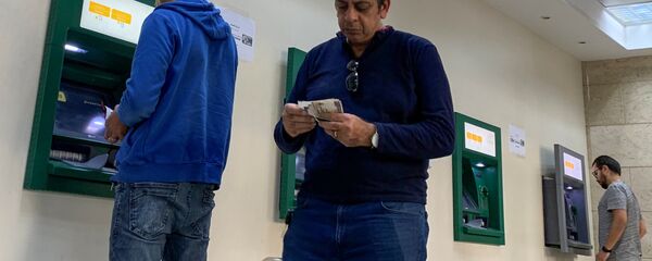 رجل يحسب أمواله بينما يستخدم الآخرون أجهزة الصراف الآلي في البنك الأهلي المصري حيث تكثف مصر جهودها لإبطاء انتشار فيروس كورونا - سبوتنيك عربي
