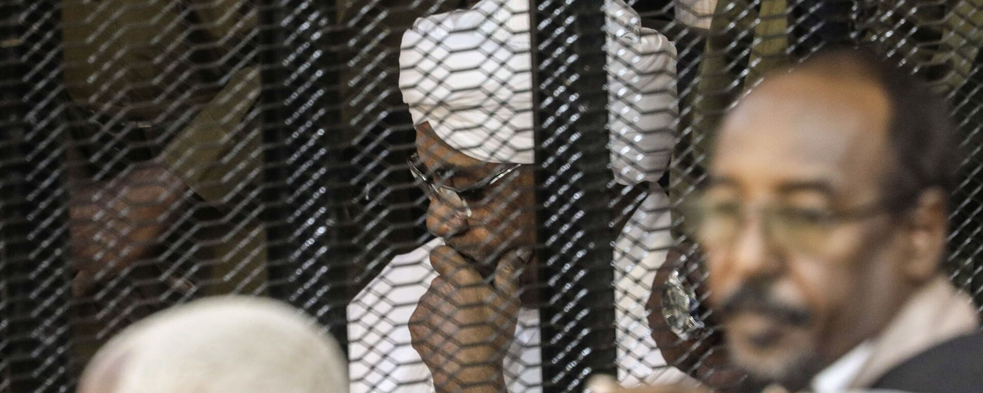الرئيس السوداني السابق عمر البشير في قفص أثناء محاكمته بتهم الفساد وغسيل الأموال في الخرطوم - سبوتنيك عربي, 1920, 26.04.2023