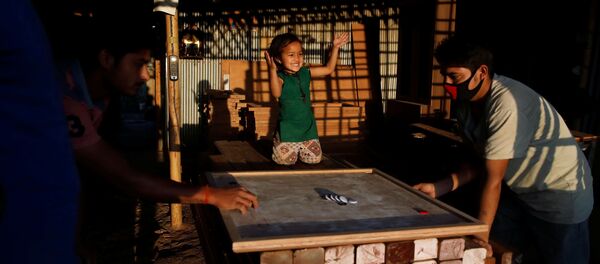 طفلة تهتف خلال لعب والدها على لوح الكيرم في ورشة أثاث خلال اليوم العاشر من الإغلاق الذي فرضته الحكومة بسبب كورونا في لاليتبور في نيبال - سبوتنيك عربي