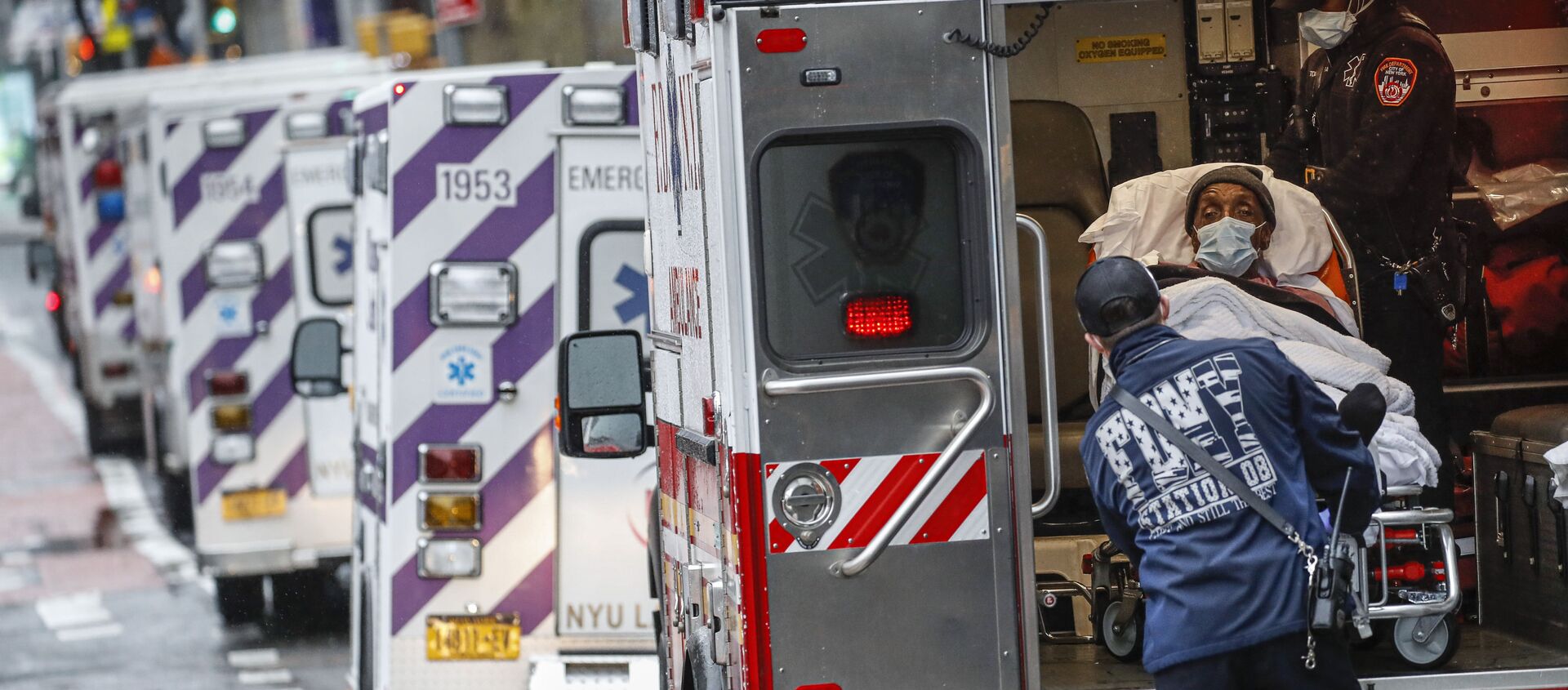 مريض يصل بسيارة إسعاف برعاية عاملين طبيين يرتدون معدات وقائية بسبب مخاوف كوفيد-19  خارج مركز جامعة نيويورك لانغون الطبي، 13 أبريل 2020 ، في نيويورك، الولايات المتحدة - سبوتنيك عربي, 1920, 31.03.2021