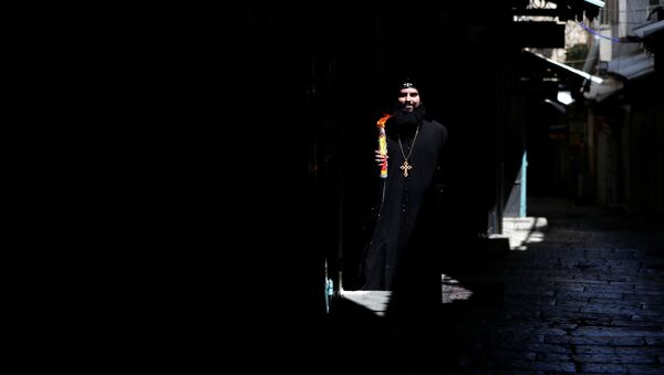 رجل دين مسيحي أرثوذكسي يحمل شموع العصا بعد احتفال النار المقدسة خارج كنيسة القيامة في البلدة القديمة في القدس وسط تفشي فيروس كورونا المستجد - سبوتنيك عربي