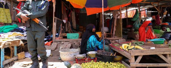 شرطي صومالي يقف على أهبة الاستعداد بينما يفرض إجراء إبعاد اجتماعي كإجراء لوقف الانتشار المتزايد لمرض فيروس كورونا (COVID-19) في مركز السوق في منطقة هاماروين في مقديشو - سبوتنيك عربي