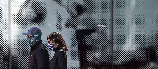 ثنائي يرتدي كمامات واقية يسيران على خلفية لوحة إعلانية لدار السينما، وسط جائحة فيروس كورونا في واشنطن العاصمة، في 22 أبريل 2020. - سبوتنيك عربي