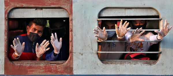 يلوح أشخاص يرتدون قفازات من القطار لدى وصولهم من ولاية تاميل نادو الجنوبية، وذلك بعد إعادة فتح محدود لخط السكك الحديدية في الهند بعد إغلاق لمدة سبعة أسابيع تقريبًا لإبطاء انتشار مرض (كوفيد-19)، في محطة سكة الحديد هوراه جانكشون على مشارف كلكتا، الهند  12 مايو 2020. - سبوتنيك عربي