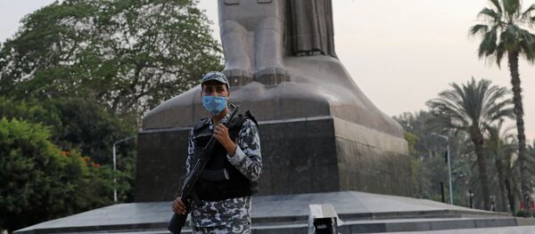 شرطي مصري يرتدي قناع وجه واقٍ يقف بجانب تمثال نهضة مصر خلال شهر رمضان حيث تكثف مصر جهودها لإبطاء انتشار فيروس كورونا - سبوتنيك عربي