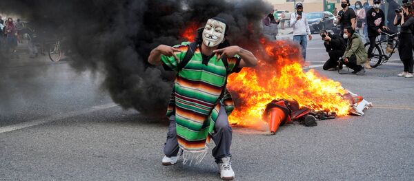 متظاهر ملثم يقف أمام حريق خلال مسيرة ضد مقتل جورج فلويد على يد شرطة مينيابوليس في لوس أنجلوس - سبوتنيك عربي