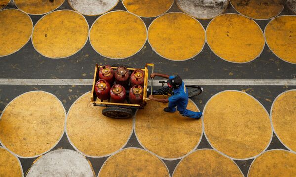 رجل يدفع عربة مملوءة بأسطوانات غاز البترول المسال في شارع فيه دوائر للمارة للحفاظ على التباعد الاجتماعي بعد تخفيف بعض القيود بعد إغلاق تام فرض لإبطاء انتشار مرض (COVID-19) في مومباي، الهند، 1 يوليو 2020. - سبوتنيك عربي