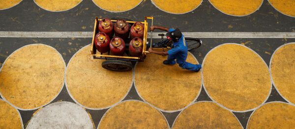 رجل يدفع عربة مملوءة بأسطوانات غاز البترول المسال في شارع فيه دوائر للمارة للحفاظ على التباعد الاجتماعي بعد تخفيف بعض القيود بعد إغلاق تام فرض لإبطاء انتشار مرض (COVID-19) في مومباي، الهند، 1 يوليو 2020. - سبوتنيك عربي