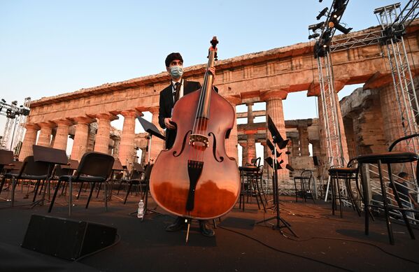 عازف تشيلو يرتدي كمامة يستعد لحفل الأوركسترا Luigi Cherubini Youth Orchestra بحضور تسعة موسيقيين من الجالبة السورية في أوروبا، من قبل الموزع والموصل الموسيقي الإيطالي ريكاردو موتي، كجزء من حفل الصداقة الرابع والعشرين، في موقع بايستوم الأثري في جنوب إيطاليا، في 5 يوليو / حزيران 2020 - سبوتنيك عربي